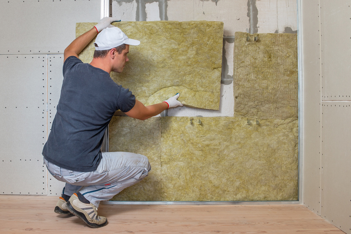 pracownik izolujący ścianę pomieszczenia izolacją termiczną